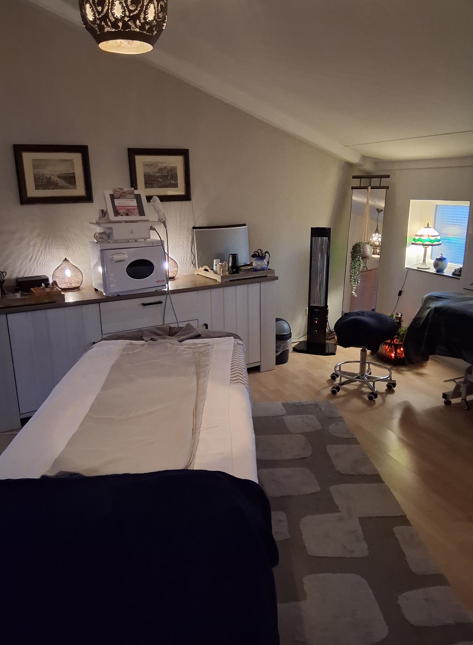 De behandelkamer van Massage Leiderdorp met de massagetafel, een kruk, ingelijste prenten en een lantaarnlamp